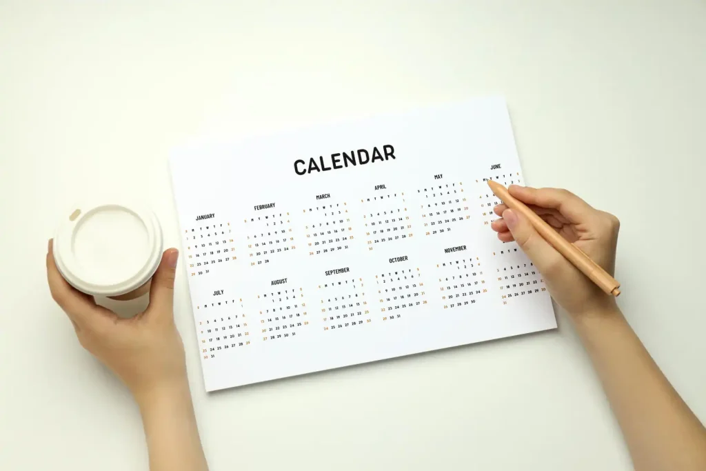 o determine what date is 28 days from today, a person holds a pencil and coffee in front of a calendar, carefully evaluating and analysing the upcoming 28-day period.